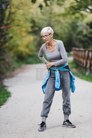 Photo for Smiling senior woman stretching before jogging in the park. Sports activities for elderly people. - Royalty Free Image