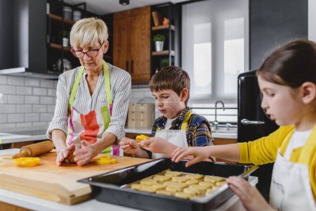 Téléchargez les photos : Mamie avec petit-fils et petite-fille faire des cookies - en image libre de droit