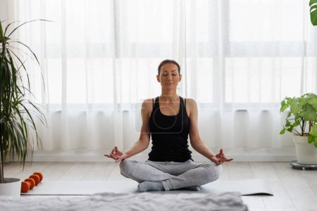 Téléchargez les photos : Jeune femme pratiquant l'exercice de yoga à la maison. Routines sportives quotidiennes pour un mode de vie sain et un soulagement du stress. - en image libre de droit