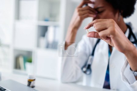 Foto de Trabajadora médica estresada trabajando en su oficina tomando pastillas - Imagen libre de derechos