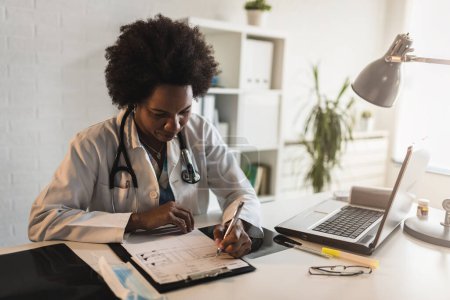 Téléchargez les photos : Femme médecin avec stéthoscope regardant les documents médicaux à son bureau travaillant dur - en image libre de droit