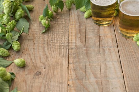 Foto de Lúpulo verde fresco con vasos de cerveza sobre fondo de madera - Imagen libre de derechos