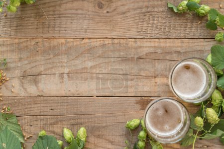 Foto de Lúpulo verde fresco con vasos de cerveza sobre fondo de madera - Imagen libre de derechos