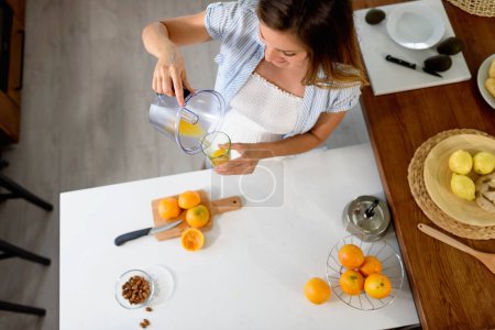 Foto de Mujer joven preparando jugo de naranja en la cocina - Imagen libre de derechos