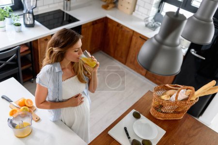 Téléchargez les photos : Photo d'une femme enceinte dans sa cuisine buvant du jus d'orange fraîchement pressé - en image libre de droit