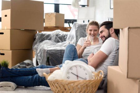 Photo for Happy young couple moving in a new home, sitting on floor drinking champagne celebrating - Royalty Free Image