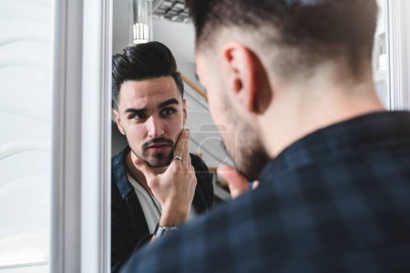 Foto de Joven hombre guapo mirando el espejo en la barbería - Imagen libre de derechos