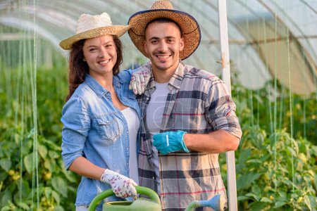 Photo for Happy young couple with watering can in greenhouse. - Royalty Free Image