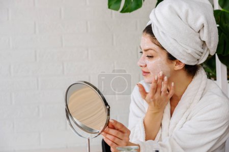 Téléchargez les photos : Belle jeune femme avec serviette sur la tête faisant routine quotidienne de soins de la peau - en image libre de droit