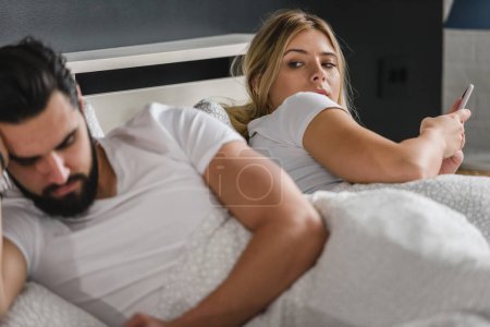 Foto de Joven pareja molesta acostada en la cama y el uso de teléfonos inteligentes - Imagen libre de derechos