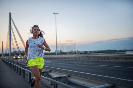 Photo for Young woman running on bridge at sunrise - Royalty Free Image