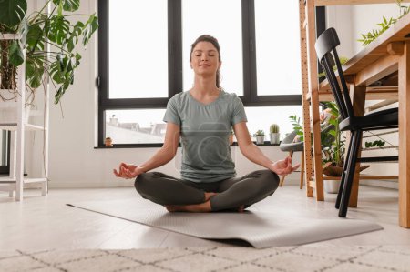 Foto de Chica atractiva haciendo ejercicios de estiramiento en casa. hermosa mujer practicando yoga y meditando. - Imagen libre de derechos