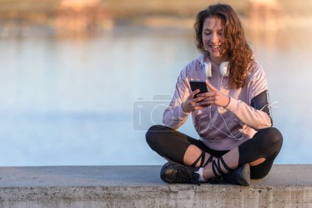 Foto de Joven corredora descansando escuchando música junto al río - Imagen libre de derechos