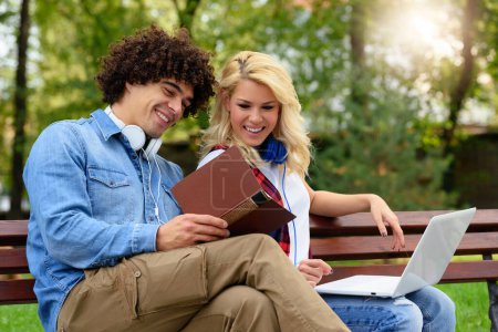 Foto de Joven pareja alegre sentada en el banco estudiando juntos en el parque - Imagen libre de derechos