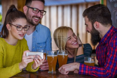 Foto de Amigos en el bar bebiendo cerveza mirando el smartphone - Imagen libre de derechos
