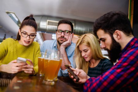 Téléchargez les photos : Des amis au bar boivent de la bière avec des smartphones - en image libre de droit
