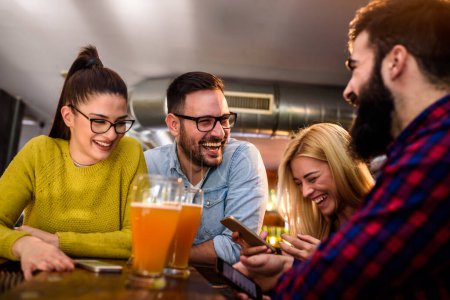 Photo for Friends at the bar drinking beer with smartphones - Royalty Free Image