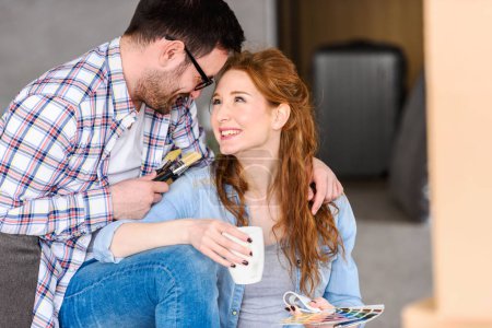 Téléchargez les photos : Jeune couple se détendre après le déballage. Choisir des couleurs pour peindre une nouvelle maison - en image libre de droit
