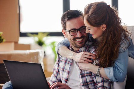 Téléchargez les photos : Couple heureux en utilisant un ordinateur portable à la nouvelle maison - en image libre de droit