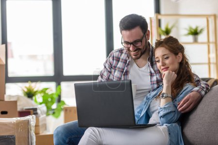 Téléchargez les photos : Couple heureux en utilisant un ordinateur portable à la nouvelle maison - en image libre de droit