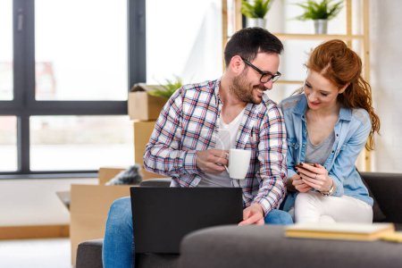 Téléchargez les photos : Heureux jeune couple à l'aide d'un ordinateur portable, déménagement à la nouvelle maison - en image libre de droit