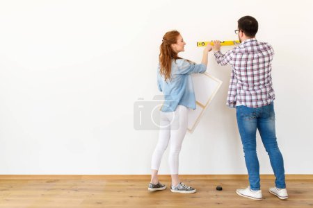 Téléchargez les photos : Couple dans un appartement vide mesurant les murs. Activités après déménagement et rénovation. - en image libre de droit