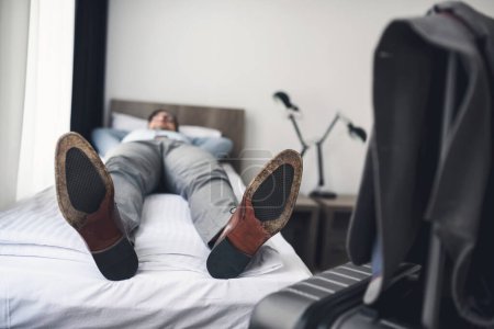 Téléchargez les photos : Homme couché sur le lit dans la chambre d'hôtel - en image libre de droit