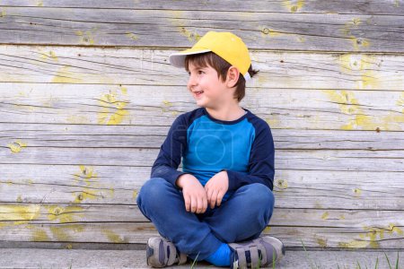 Photo for Happy boy in a yellow hat sitting against wooden background - Royalty Free Image