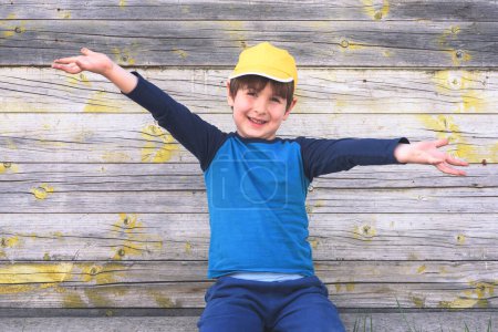 Téléchargez les photos : Heureux garçon dans un chapeau jaune assis sur fond en bois - en image libre de droit