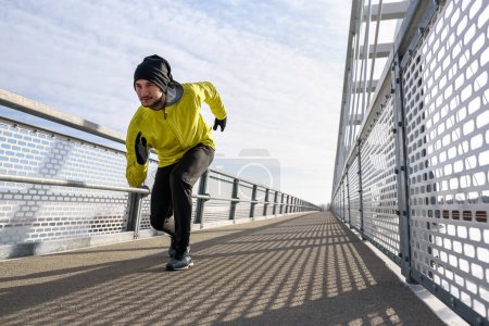 Photo for Attractive fit man running fast along big modern bridge. Exercising, Jogging, Sport, Winter. Male athlete running. - Royalty Free Image
