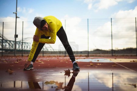 Photo for Young athlete man stretching his muscles before running on bridge on a rainy day - Royalty Free Image