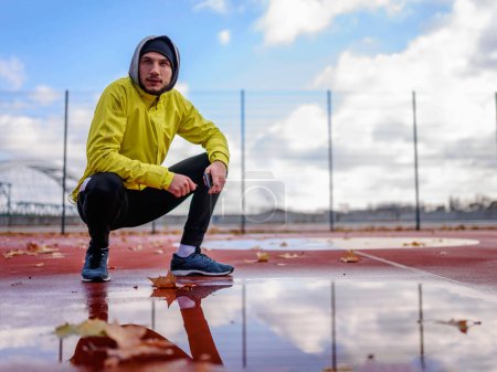 Téléchargez les photos : Portrait d'un jeune athlète en coupe-vent utilisant un téléphone intelligent lors d'une journée ensoleillée d'hiver - en image libre de droit