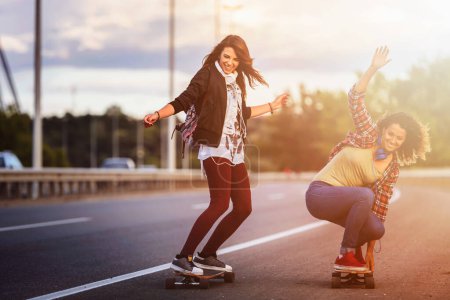 Téléchargez les photos : Jeunes femmes heureuses chevauchant sur des planches à roulettes dans les rues de la ville - en image libre de droit