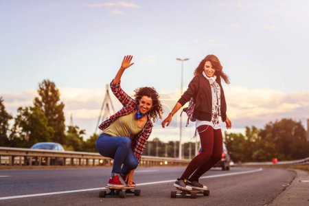 Foto de Mujeres jóvenes felices montando en monopatines en las calles de la ciudad - Imagen libre de derechos