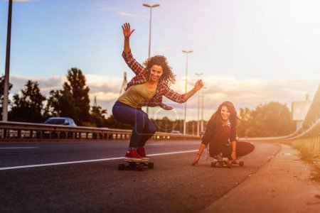 Téléchargez les photos : Jeunes femmes heureuses chevauchant sur des planches à roulettes dans les rues de la ville - en image libre de droit