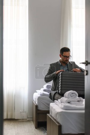 Téléchargez les photos : Homme d'affaires assis dans sa chambre d'hôtel déballer - en image libre de droit