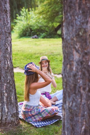 Téléchargez les photos : Deux amies assises sur l'herbe, parlant et utilisant un ordinateur portable - en image libre de droit