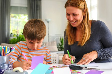 Téléchargez les photos : Fière mère enseignant à son enfant à la maison comment écrire. Éducation préscolaire - en image libre de droit