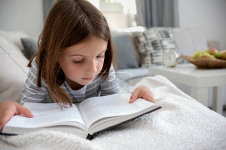 Photo for Beautiful little girl reading book on sofa - Royalty Free Image