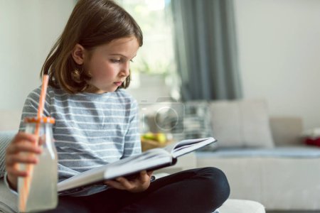 schönes kleines Mädchen liest Buch auf dem Sofa 