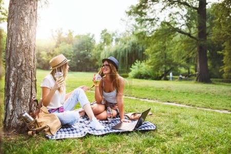 Photo for Girls friends sitting in park on blanket talking, drinking lemonade - Royalty Free Image