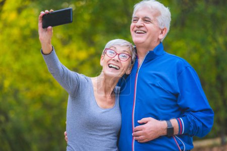 Téléchargez les photos : Sourire couple aîné dans le parc prendre selfie - en image libre de droit