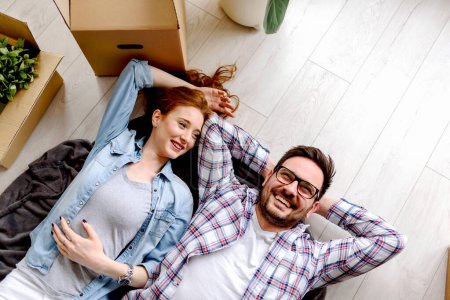 Photo for Beautiful young couple lying on the floor among cardboard boxes in their new apartment they just moved in. Daydreaming, making plans for the future. - Royalty Free Image