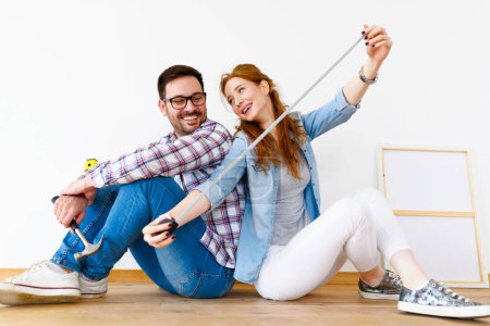 Photo for Beautiful couple just moved into new empty apartment sitting on the floor with ruler. Activities after relocation. Renovating property. - Royalty Free Image