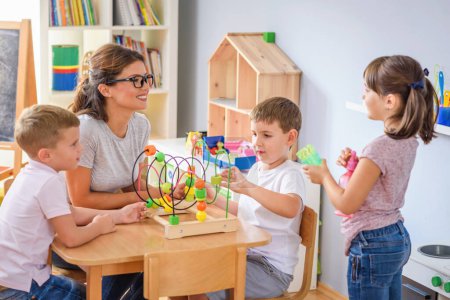 Photo for Preschool teacher with children playing with colorful wooden didactic toys at kindergarten - Royalty Free Image