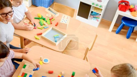 Photo for Teacher playing with kids in kindergarten using wooden blocks - Royalty Free Image