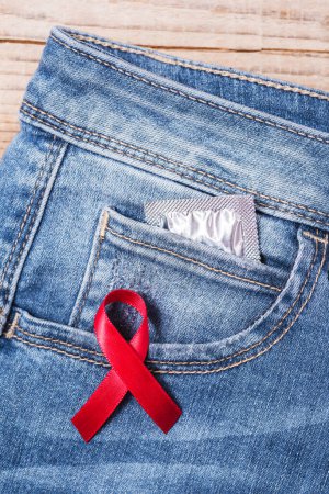 Téléchargez les photos : Ruban rouge sur denim bleu avec préservatif dans la poche - en image libre de droit