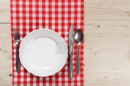 Photo for Wooden Table with Checkered Red Tablecloth Plate Fork and Knife - Royalty Free Image
