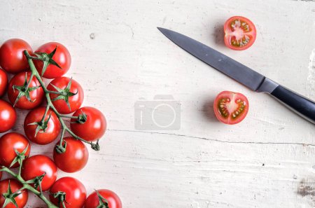 Téléchargez les photos : Bouquet de tomates cerises rouges coupées avec couteau de cuisine sur une vieille table blanche - en image libre de droit