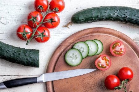 Téléchargez les photos : Concombre et tomates coupées avec un couteau de cuisine sur une vieille table blanche - en image libre de droit